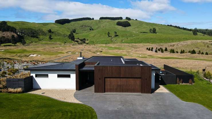 guy pushing golf cart in front of modern black house  210 Oceanbeach Road, MOunt Maunganui