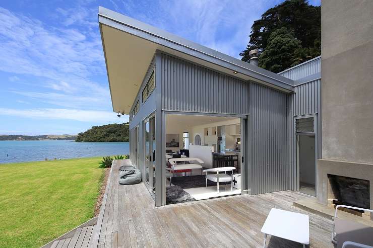 345 Gordons Road, Waiheke Island, Auckland. Grey roofed modern house with deck and lawn overlooking ocean.