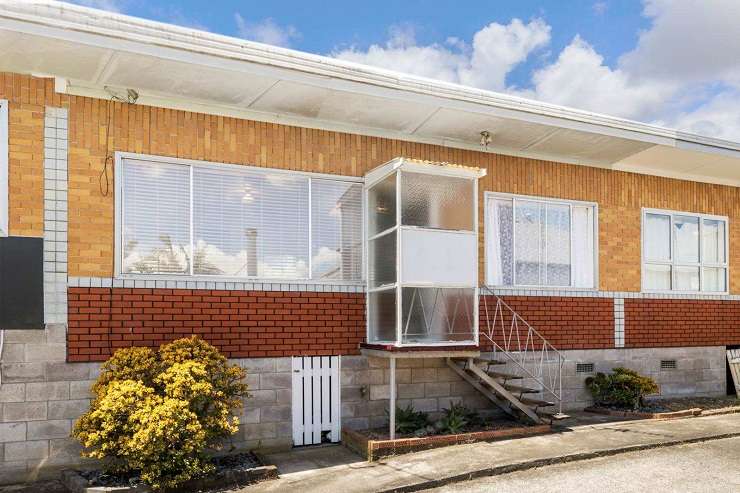 50A waiatarua Road remuera  1950s brick house with red door and sofas on front porch lit up at night