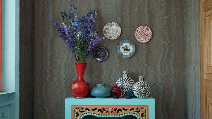 red vase, flowers, three plates on wall, decorative bottles on fancy table