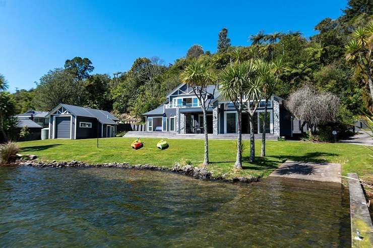 47 Wharetoroa Drive, Lake Rotoiti, Rotorua  a modern black lodge building on a green lawn next to a lake and dock